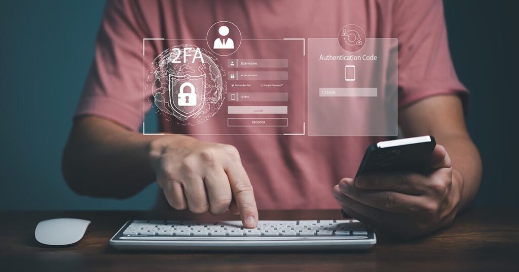 A man with a red shirt with his face cropped out holding his phone and typing on a keyboard with 2FA authentication code prompts super imposed on the image.