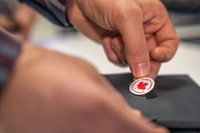 A person of colour placing a Made in Canada sticker on an item they have produced.